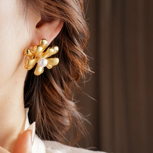 Detailed view of an 18k gold plated flower earring with a white pearl on an ear