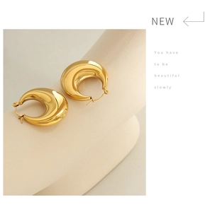 Detailed view of chunky U-shape gold earrings with a polished mirror finish on a pedestal