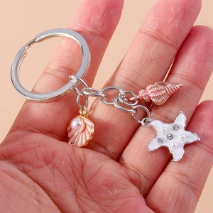 Detail of a pearl starfish keychain with pink shells and rhinestones held by a hand
