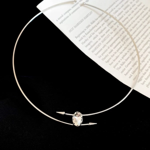 Close-up of silver metal choker with oval crystal and arrow-shaped ends on black velvet
