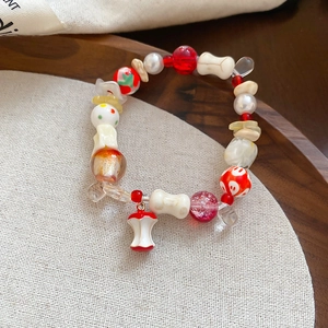 Detail of beaded bracelet featuring ceramic apple pendant and red mushroom charms