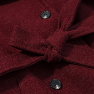 Detailed close-up of wine red wool coat fabric texture with belt knot and dark buttons