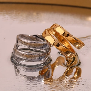 Macro shot of 18K gold and silver double-layered crisscross rings on a reflective surface