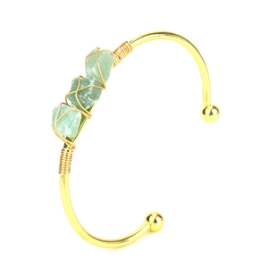 Detail of green raw stones wrapped in gold wire on a handmade open bangle bracelet