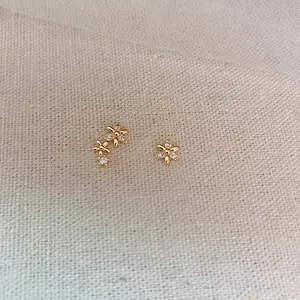 Minimalist gold flower stud earrings with zircon inlay displayed on a beige linen background