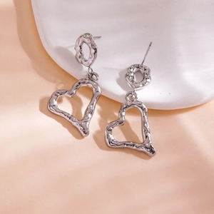 Modern silver heart drop earrings with irregular hammered texture on a white display pedestal