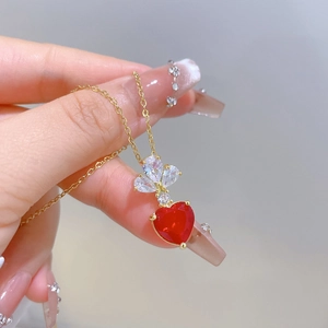Detailed close-up of a gold necklace featuring a red heart stone and clear zircon leaves