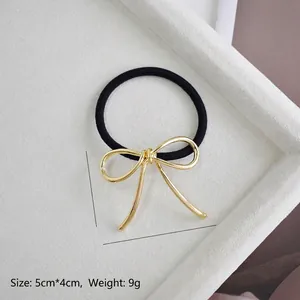 Close-up of golden alloy bow pendant on black elastic hair tie with 5cm size detail