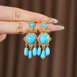Detail of vintage gold-tone earrings with blue resin stones held by hand to show size