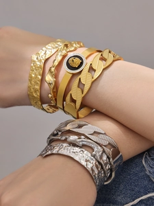 Detail of layered gold and silver textured bangles with a lion head disc on a model arm