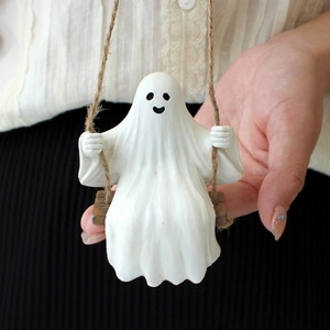 Detail of white ghost figurine on wooden swing with jute rope for outdoor garden decor