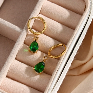 Primer plano de aretes de aro dorados con gemas verdes sobre terciopelo beige suave