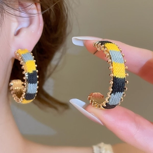 Detail of C-shaped earrings with yellow, grey and black knit texture and golden edges