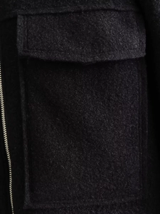 Detailed macro view of black wool coat featuring textured fabric with pocket and metal zipper
