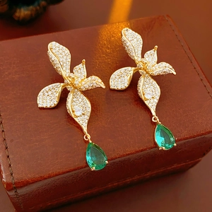 Detail of vintage gold flower earrings with white zircon petals and green teardrop gems