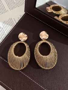 Close-up of gold oval woven hollow earrings on dark brown leather storage box