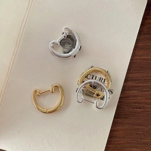 Close-up of minimalist gold and silver polished C-shape hoop earrings on a textured card