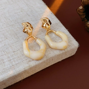 Close-up of golden oval resin earrings with cream marble texture on a linen surface