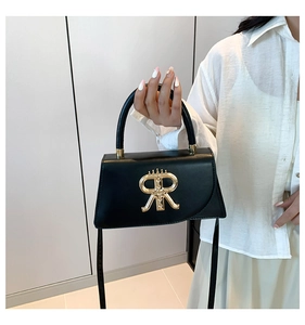 Detail of black leather handbag featuring a golden RR crown emblem held by a model