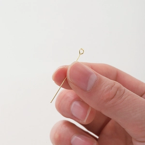 Macro detail of 18K gold-plated eye pin held by hand for scale in jewelry making