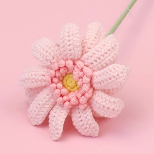Nahaufnahme einer handgehäkelten rosa Gerbera-Blume mit realistischer Garntextur und grünem Stiel