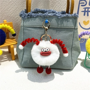 Detail of cute white plush monster keychain with red horns on a blue denim bag