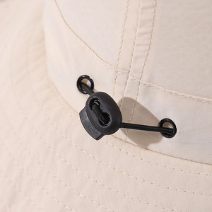 Detail of adjustable drawstring toggle on kid's fisherman hat with beige fabric texture