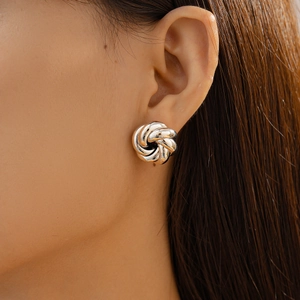 Close-up of polished silver metal love knot stud earring worn by a model