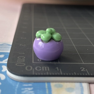 Vista macro di un ciondolo a mangostano in resina viola da 1cm su tappeto graduato