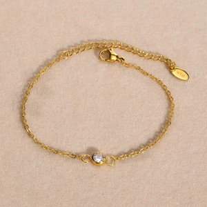 Detail of minimalist gold chain bracelet with K18 engraving and clear zircon stone