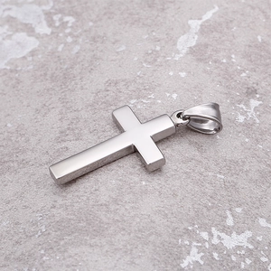 Detailed view of a polished silver stainless steel cross pendant on a textured grey surface