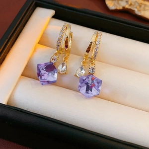 Detail of gold earrings featuring purple crystal cubes and sparkling zircon stones