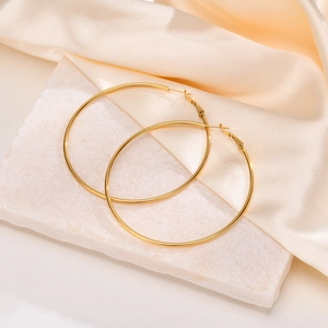 Close-up of gold oversized hoop earrings on marble and satin fabric background
