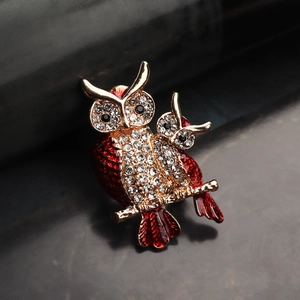 Macro detail of red enamel and crystal owl brooch on a golden branch against dark background