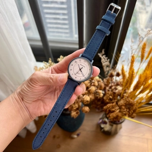 Close-up of minimalist quartz watch with dark blue suede strap and beige dial in natural light