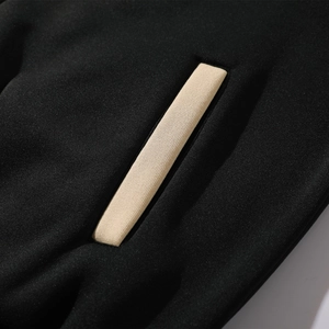 Macro shot of contrast beige rib trim on pocket edge of black baseball jacket