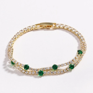 Close-up of double-row gold tennis bracelet with white cubic zirconia and green gemstones