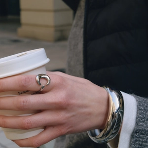 Close-up of polished silver steel ring and wide bangle set held with a coffee cup
