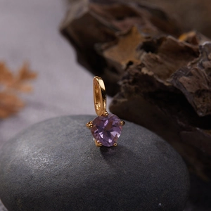 Macro shot of a heart-shaped purple gemstone pendant on a rustic natural stone background