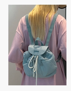 Rear view of a light blue nylon drawstring backpack with front pockets on a model