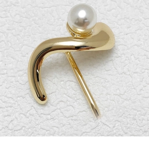 Detailed close-up of a golden curved ponytail clip featuring a white pearl inlay on a white surface