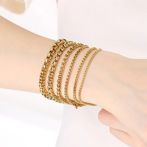 Multiple layered gold box chain bracelets in various widths on model wrist