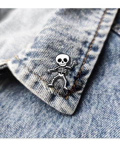 Cute cartoon skeleton enamel pin badge displayed on a blue denim jacket collar