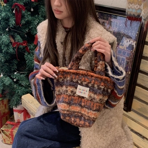 Detail view of colorful knitted plush handbag featuring a brand label in a warm winter setting