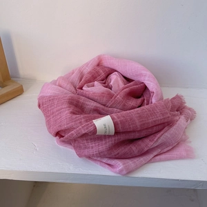 Artistic detail of a pink gradient cotton linen scarf folded into a rose shape with tassels