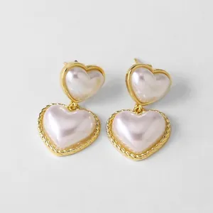 Detalle de aretes de doble corazón dorado con incrustación de perla y borde trenzado