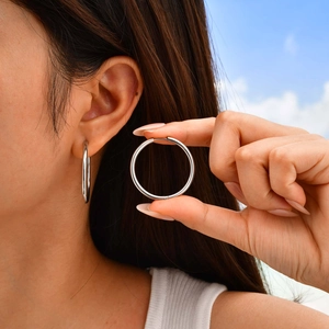 Polished silver stainless steel hoop earring shown on ear under bright natural sunlight