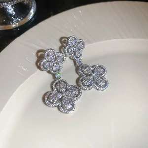 Detailed close-up of clover flower earrings with silver metal and zircon inlay on a ceramic plate