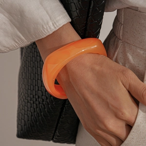 Close-up of vibrant orange resin bangle on wrist with stylish textured background