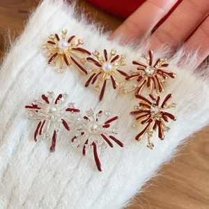 Detail of fireworks stud earrings with red enamel and pearls on soft white fabric background